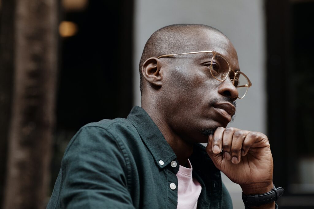 Close up shot of a black man who is deep in thought, employing the skills he learned in solution focused therapy at Delia Counseling Services to overcome negative thoughts.