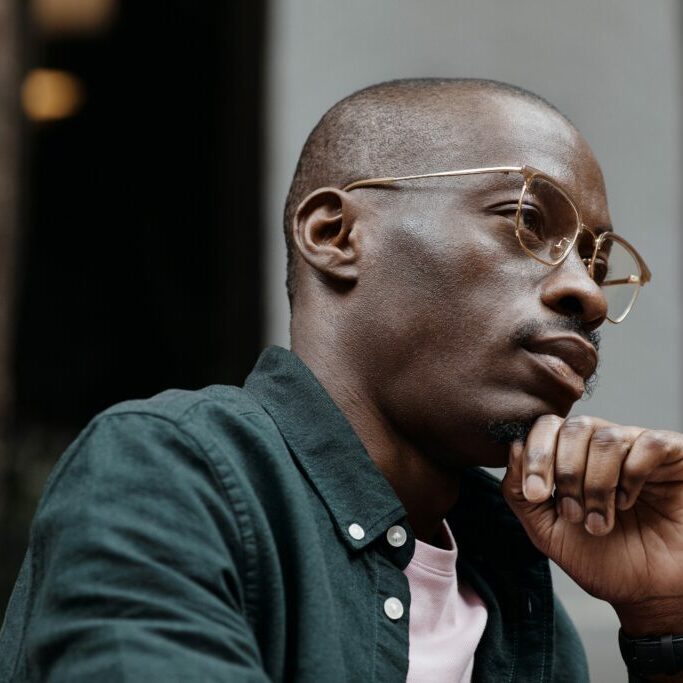 Close up shot of a black man who is deep in thought, employing the skills he learned in solution focused therapy at Delia Counseling Services to overcome negative thoughts.